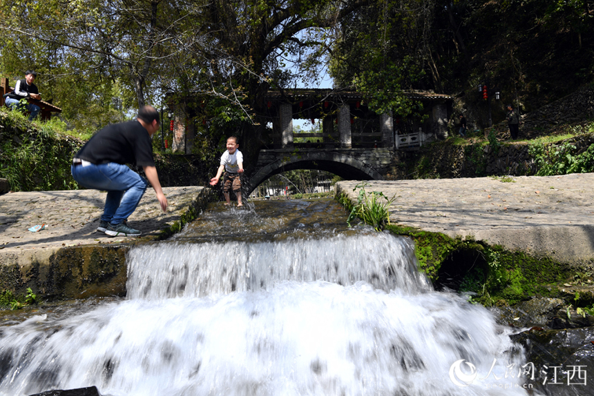 小朋友和家長在古村旁的溪流里嬉戲。人民網 時雨攝