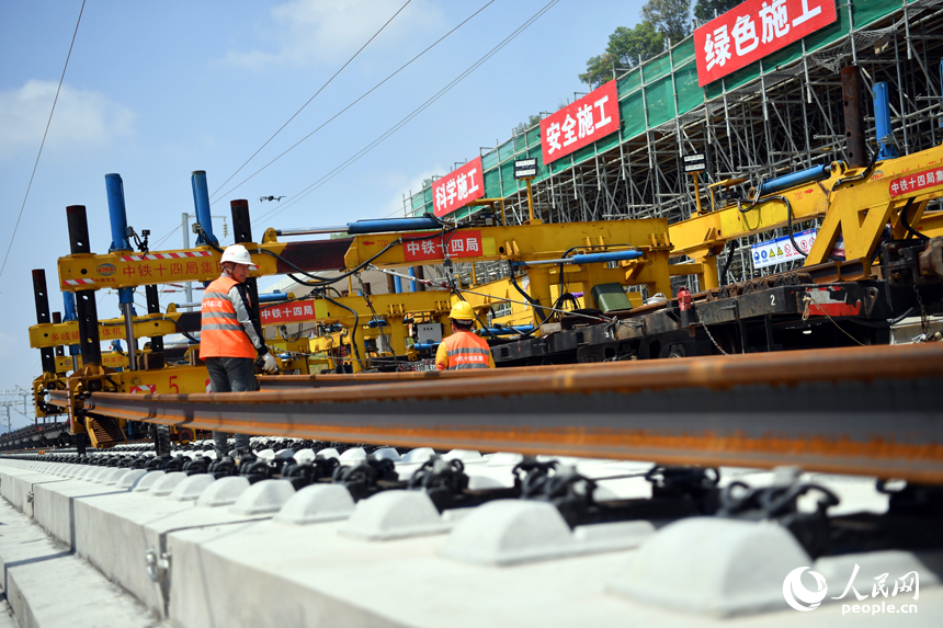 浮梁東站內多線鋪軌一體機正在將鋼軌鋪入無砟軌道承軌槽中。 人民網記者 時雨攝