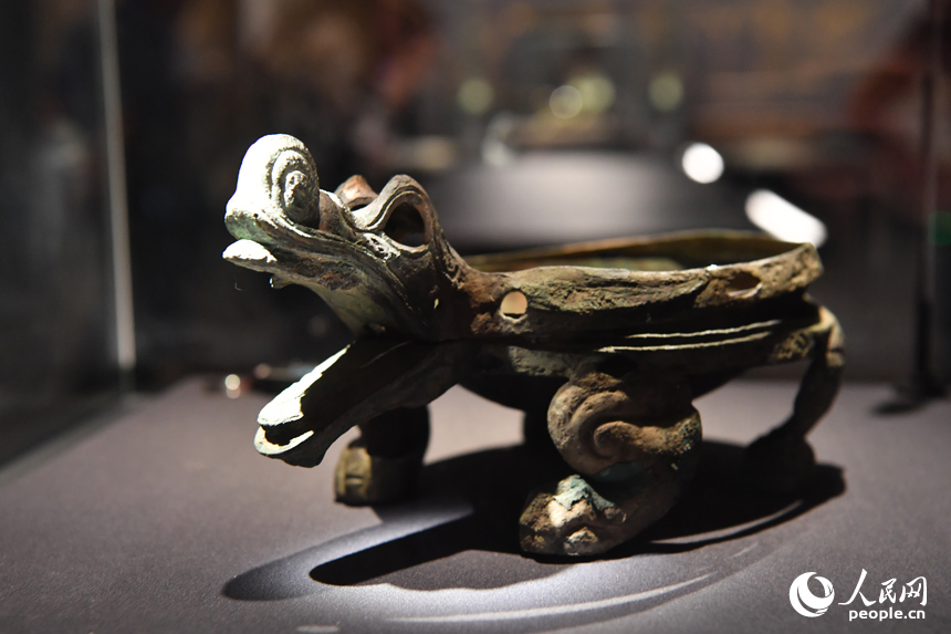 鎏金鑲玉龍首四足青銅匜。該器呈圓形，前有流，龍首狀，四獸足粗壯扁平，器身鎏金并鑲嵌玉石，由底座、青銅盆及蓋三部分組成，造型獨特，鑄造精美。匜，古代洗手注水用具。人民網記者 時雨攝