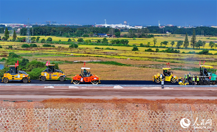 工人在加緊鋪設瀝青路面，一片繁忙施工景象。人民網 朱海鵬攝