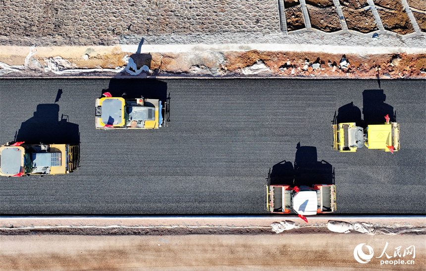 工人在加緊鋪設瀝青路面，一片繁忙施工景象。人民網 朱海鵬攝