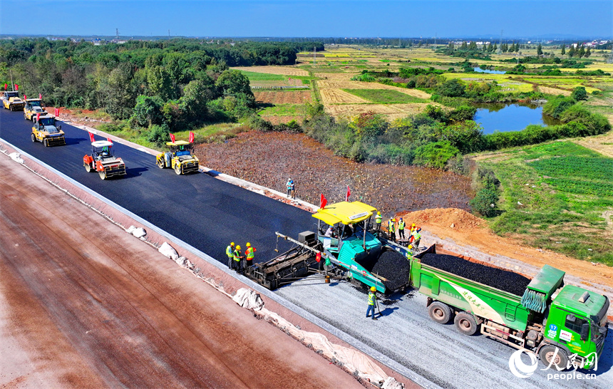 工人在加緊鋪設瀝青路面，一片繁忙施工景象。人民網 朱海鵬攝