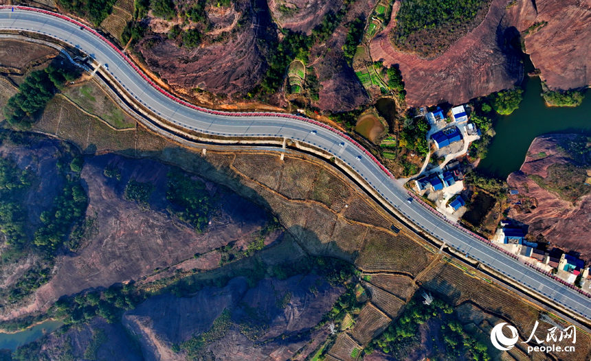 上饒市弋陽縣圭峰鎮，車輛在蜿蜒的公路上穿行，與沿線丹霞地貌山丘相映成景。人民網 朱海鵬攝