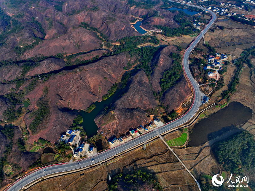 上饒市弋陽縣圭峰鎮，車輛在蜿蜒的公路上穿行，與沿線丹霞地貌山丘相映成景。人民網 朱海鵬攝