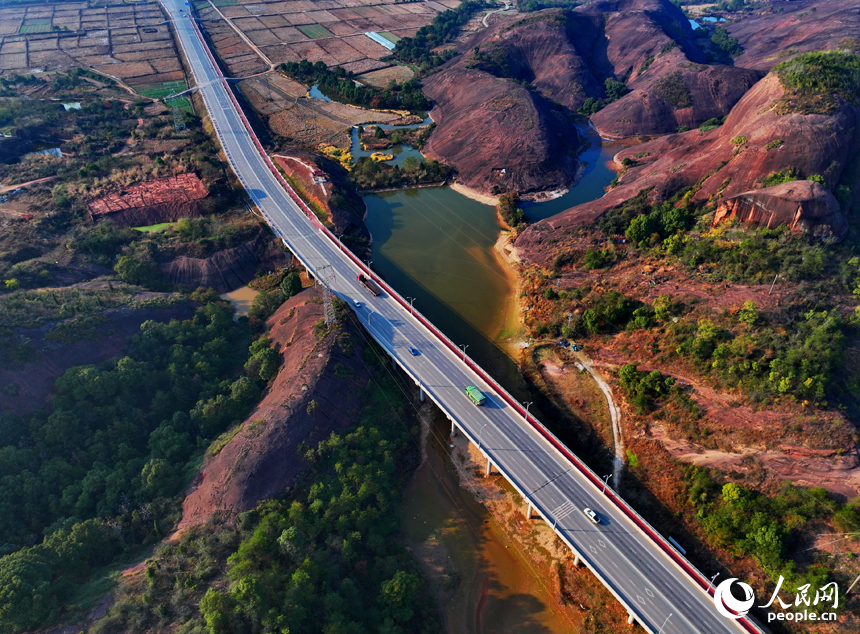 上饒市弋陽縣圭峰鎮，車輛在蜿蜒的公路上穿行，與沿線丹霞地貌山丘相映成景。人民網 朱海鵬攝