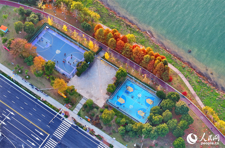 吉安市吉水縣贛江沿岸的一處“口袋公園”，許多市民在打籃球，色彩斑斕的樹木與籃球場、健身步道、碧綠江水相映襯。人民網 朱海鵬攝