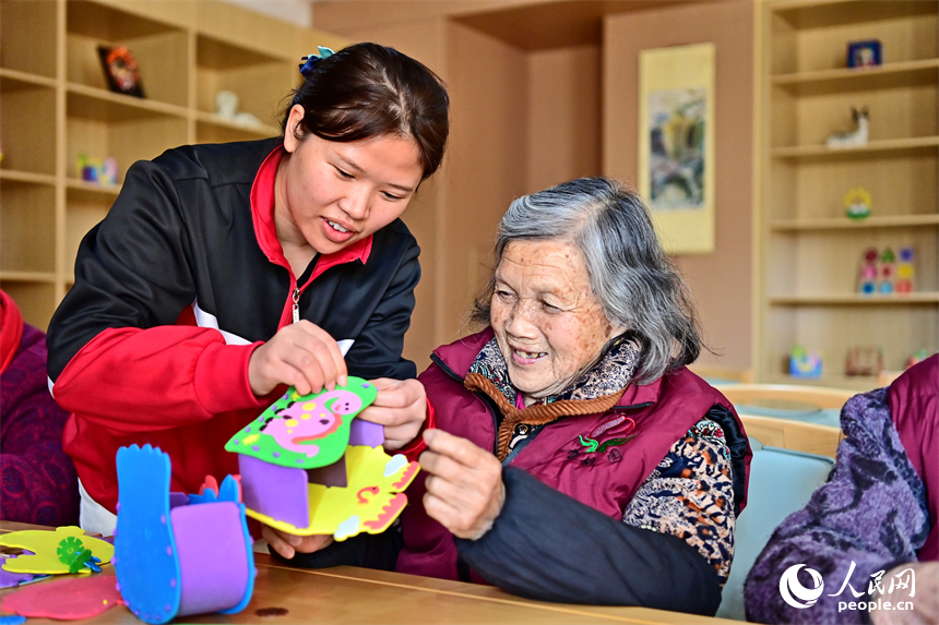 贛州市南康區蟠桃園老年公寓，護工在陪伴老人制作手工擺件。人民網 朱海鵬攝