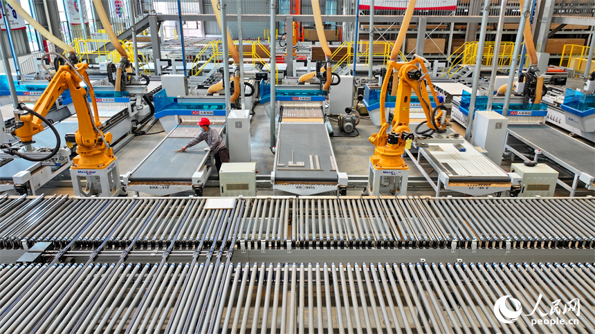 南康區的一家全屋定制家具生產企業智能制造車間內，工人在自動化生產線上調控智能機械臂加工板材。人民網 朱海鵬攝