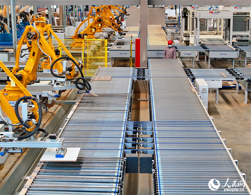 南康區的一家全屋定制家具生產企業智能制造車間內，工人在自動化生產線上調控智能機械臂加工板材。人民網 朱海鵬攝