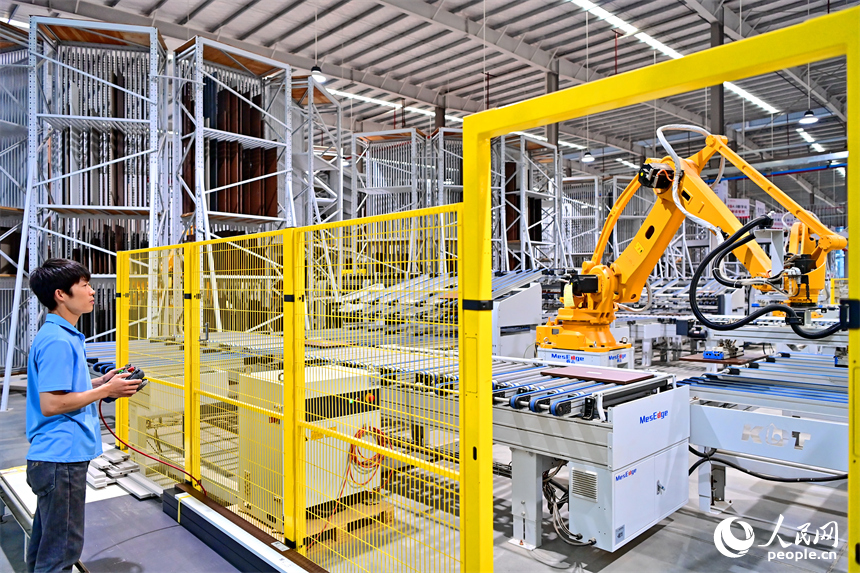 贛州市南康區國際家居總部經濟區的一家企業全屋整裝智能制造車間內，工人在操作智能機器人手臂裁切家具板材。人民網 朱海鵬攝