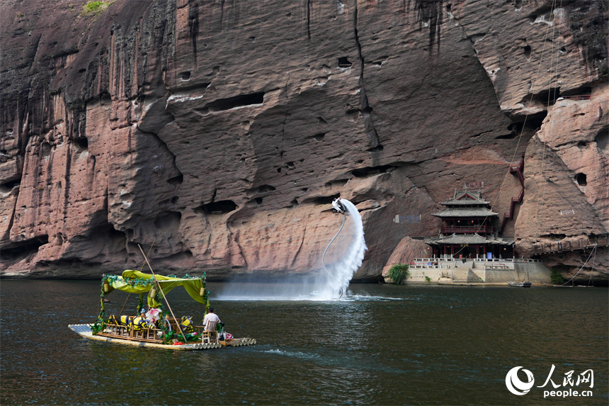 丹霞巖壁與碧水相映，游客坐在竹筏上欣賞山水奇峰。人民網 涂詩軒攝