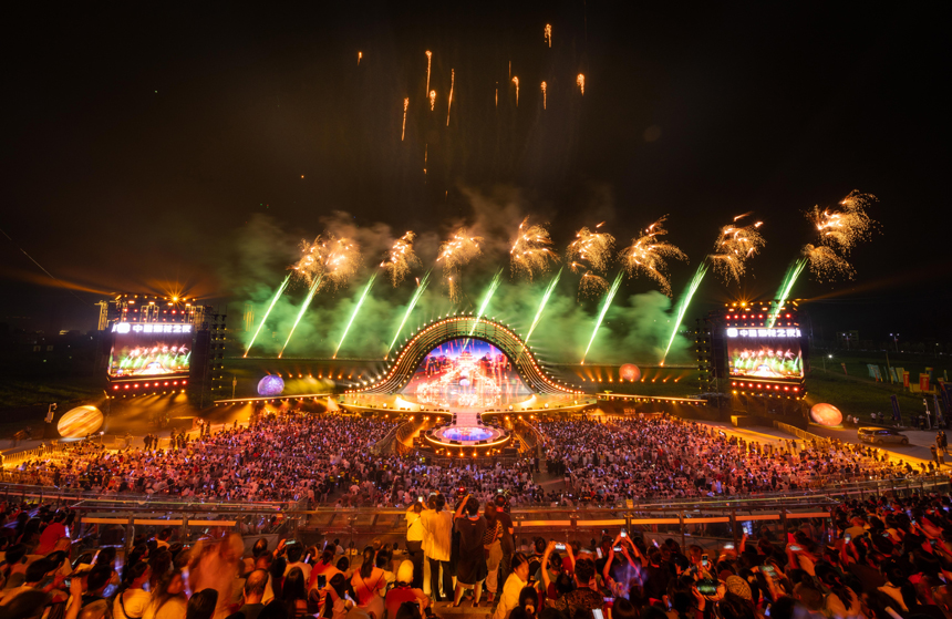 夜空綻放的絢爛煙花與下方燈火璀璨的舞臺、觀眾交相輝映。 顏紹明攝